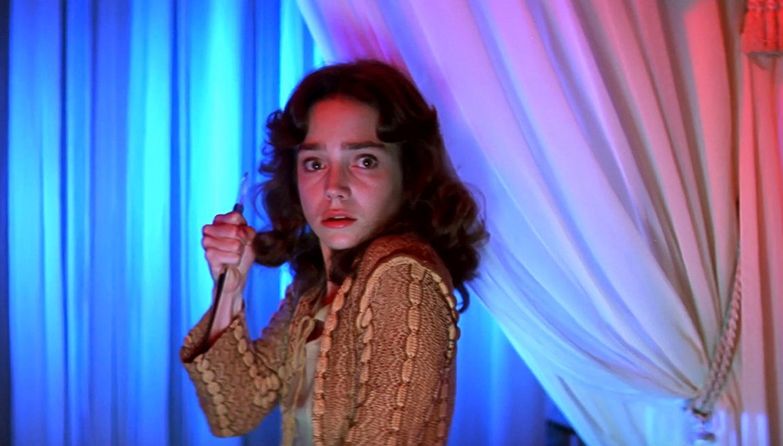 Suzy from Suspiria holding a knife, looking afraid, standing in front of curtains lit with blue and red light
